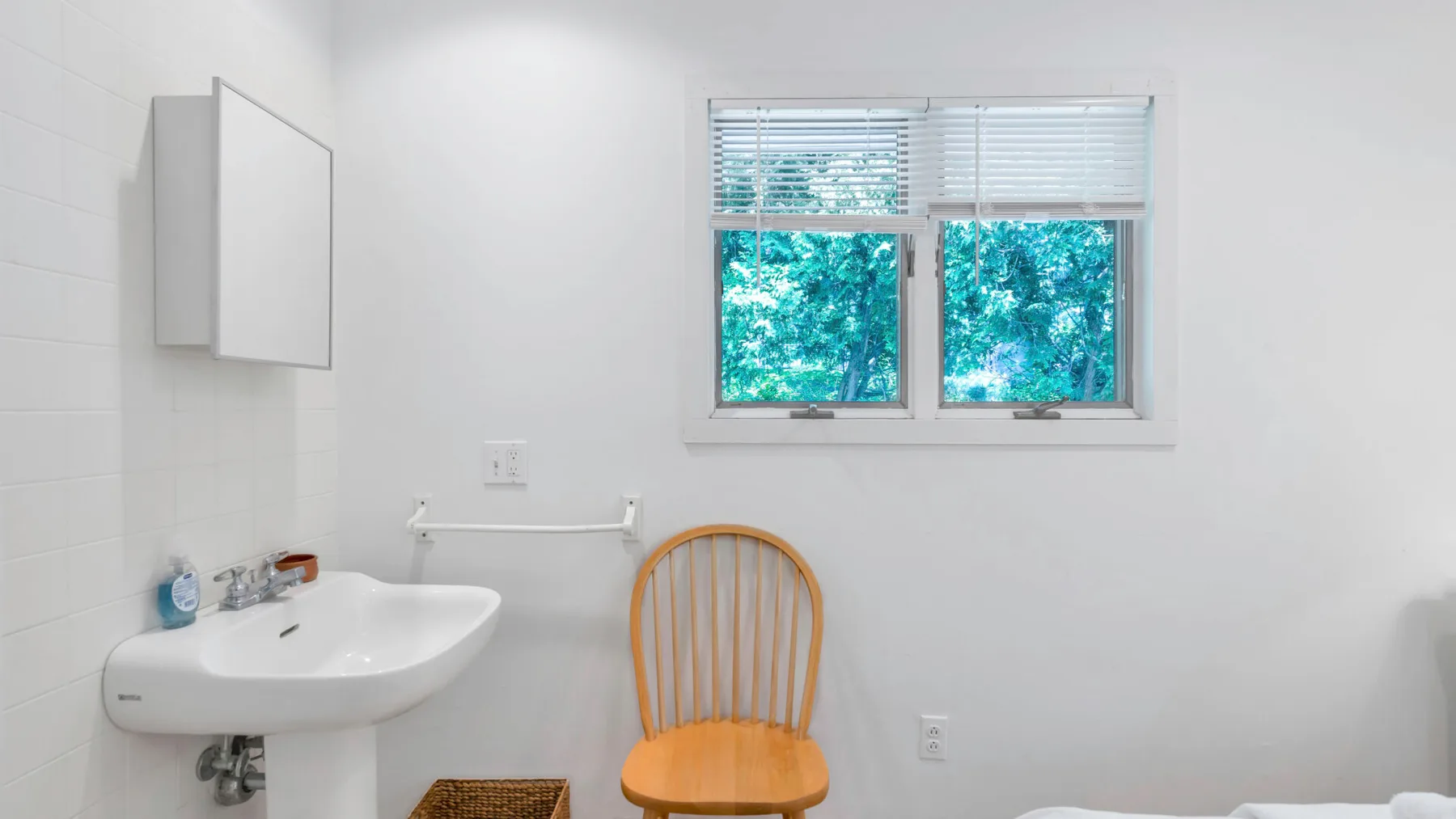 Un baño luminoso con lavabo de pared y una ventana con vistas a la vegetación.