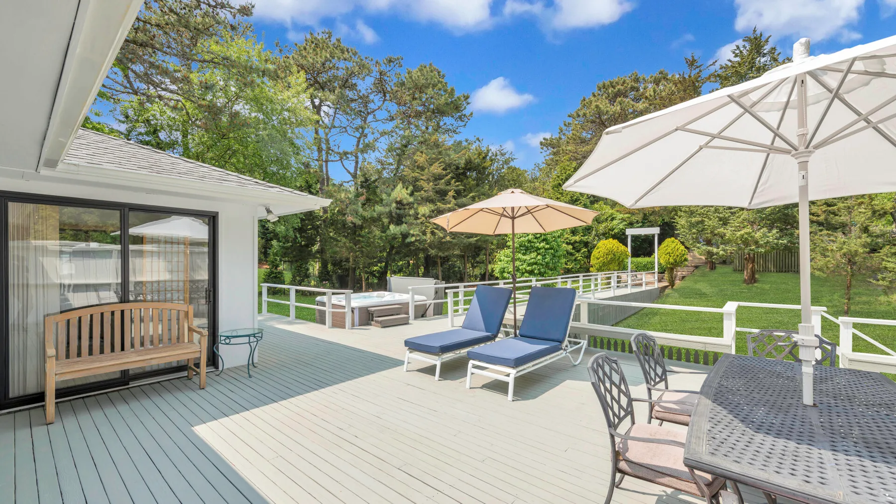A sunny outdoor deck with lounge seating, patio umbrellas, and a white railing.