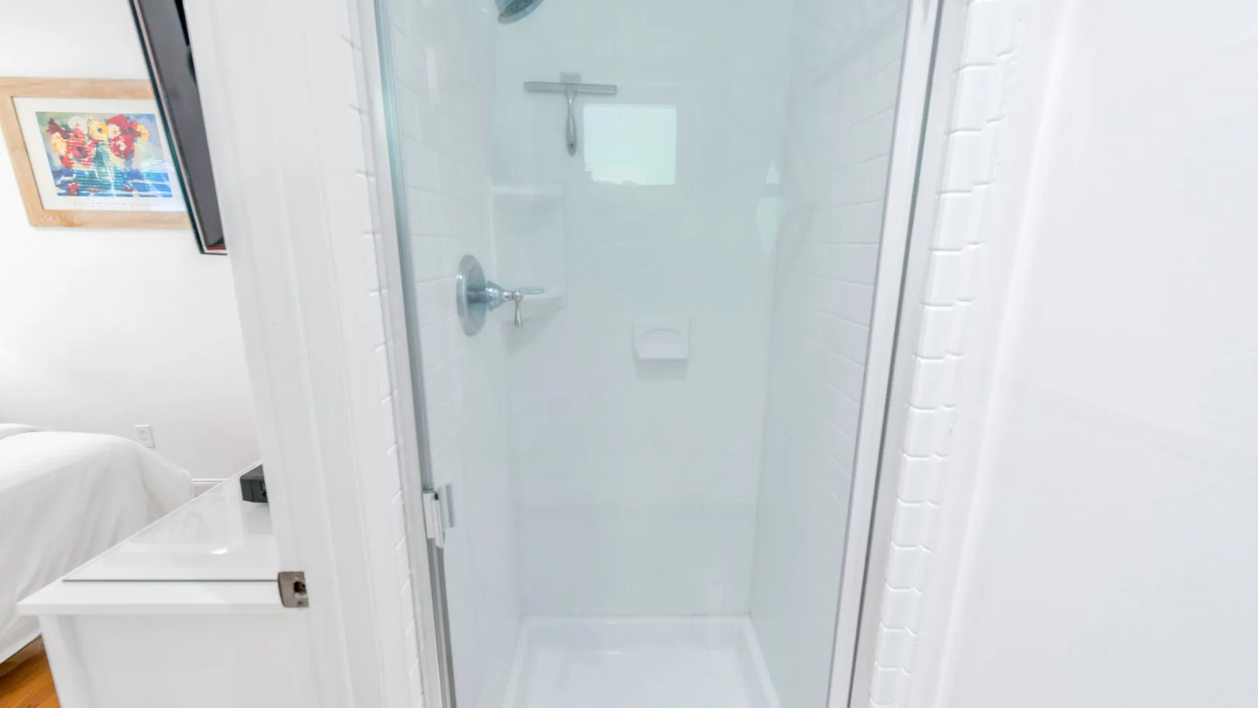 Una ducha de baño con paneles de vidrio transparente y paredes de azulejos blancos.
