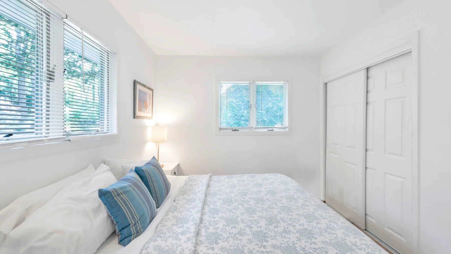 Un dormitorio luminoso con una cama hecha y ventanas con persianas.