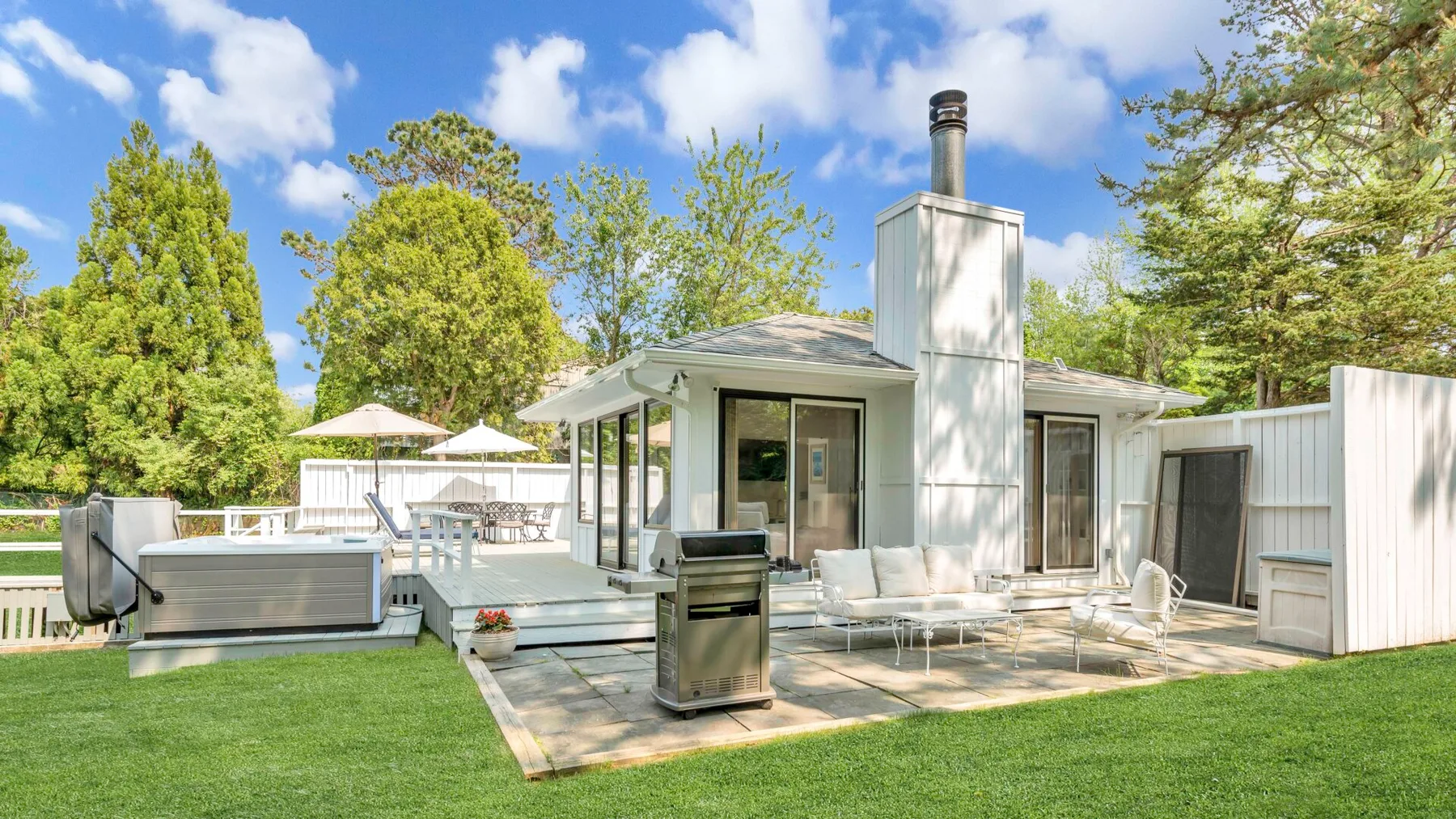 Un patio junto a una casa blanca, con asientos al aire libre y una parrilla.