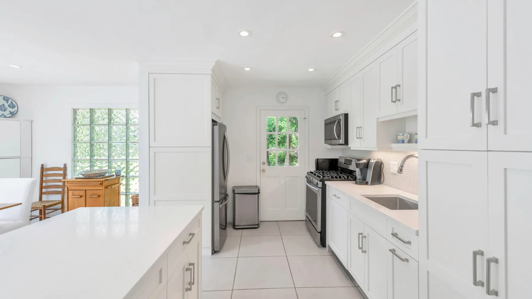 Una cocina blanca y luminosa con una isla central y electrodomésticos de acero inoxidable.