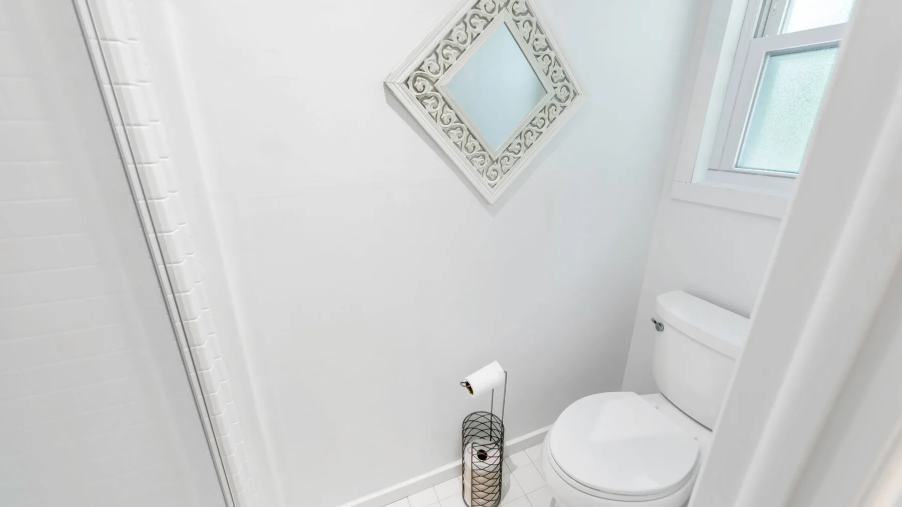 Un baño luminoso con un inodoro y un pequeño espejo en forma de rombo.