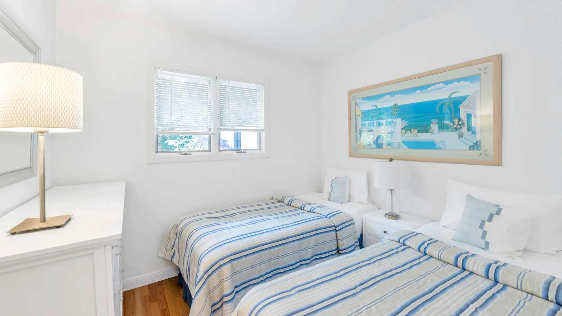Un dormitorio luminoso con dos camas vestidas con ropa de cama a rayas azules y blancas.