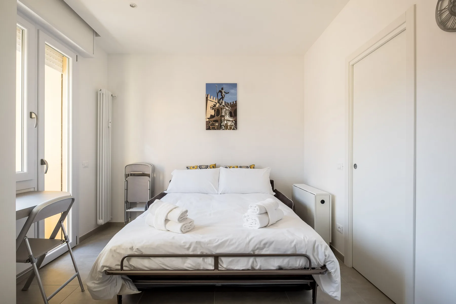A bright bedroom with a neatly made bed beneath a small wall picture.