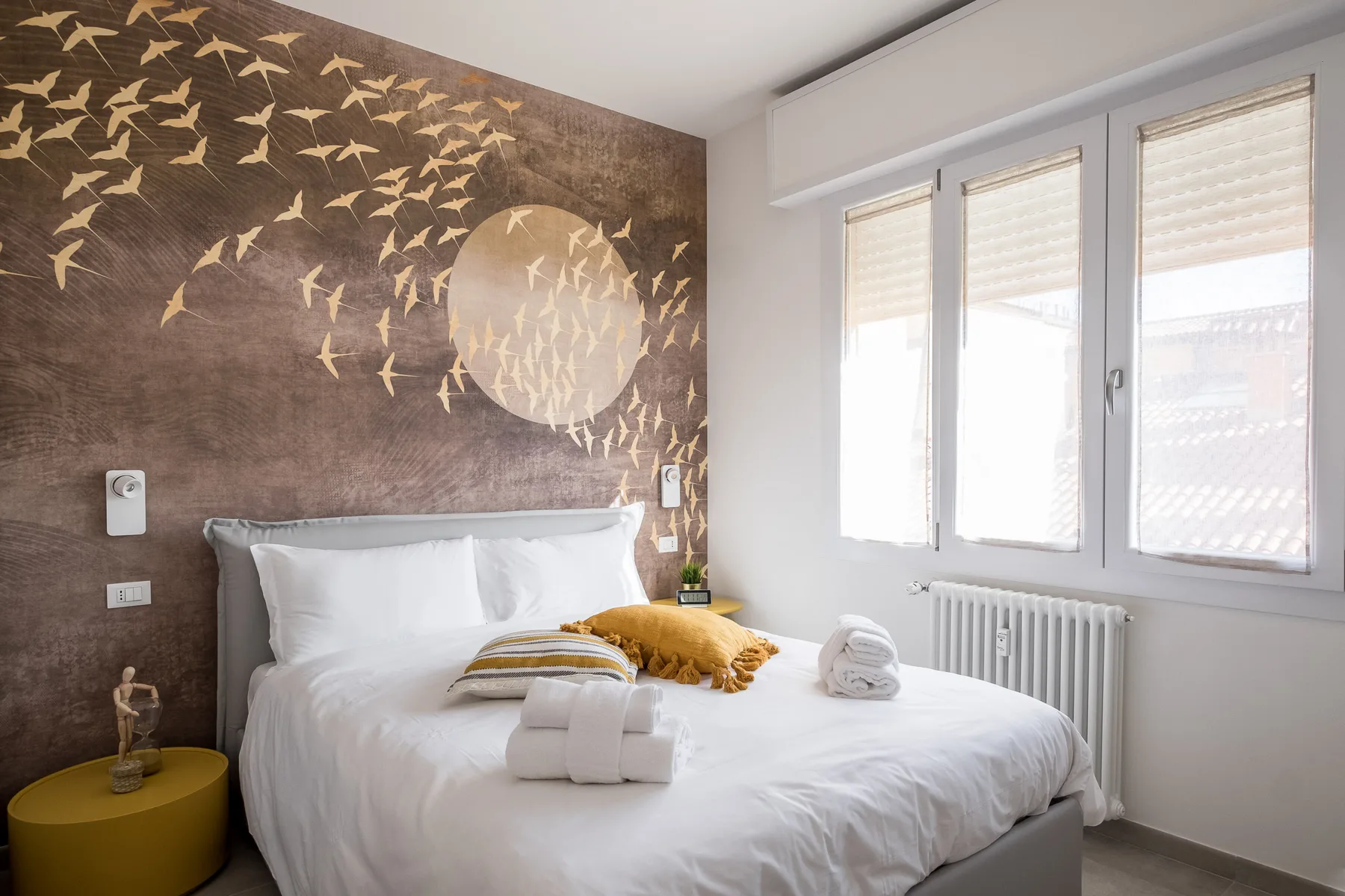 A bedroom with a white bed beneath a decorative bird-patterned wall.