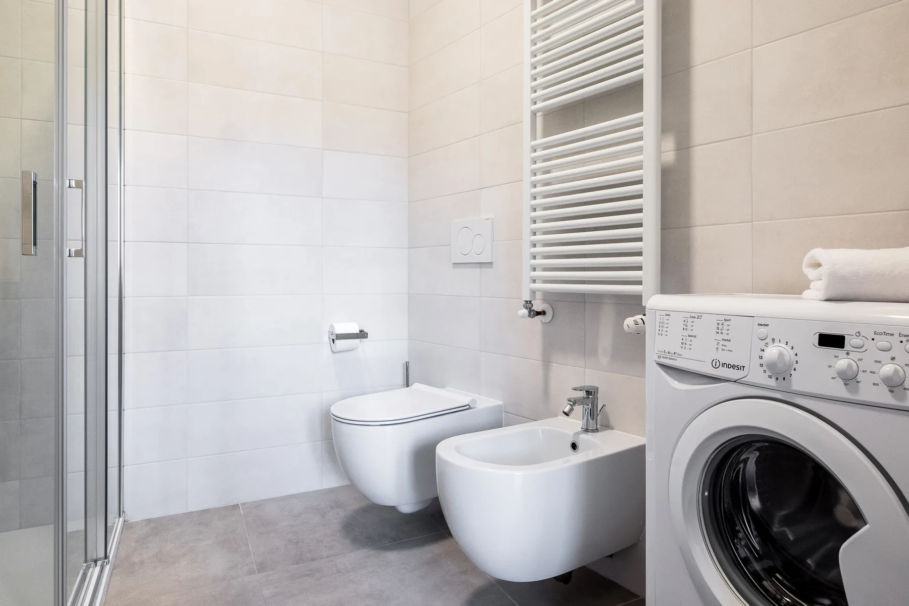 A tiled bathroom with a shower, toilet, bidet, and washing machine.