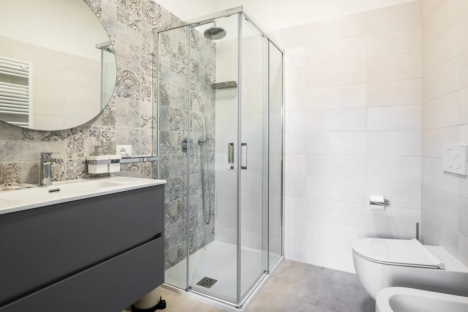 A bright bathroom with a glass shower, vanity, and white tiled walls.