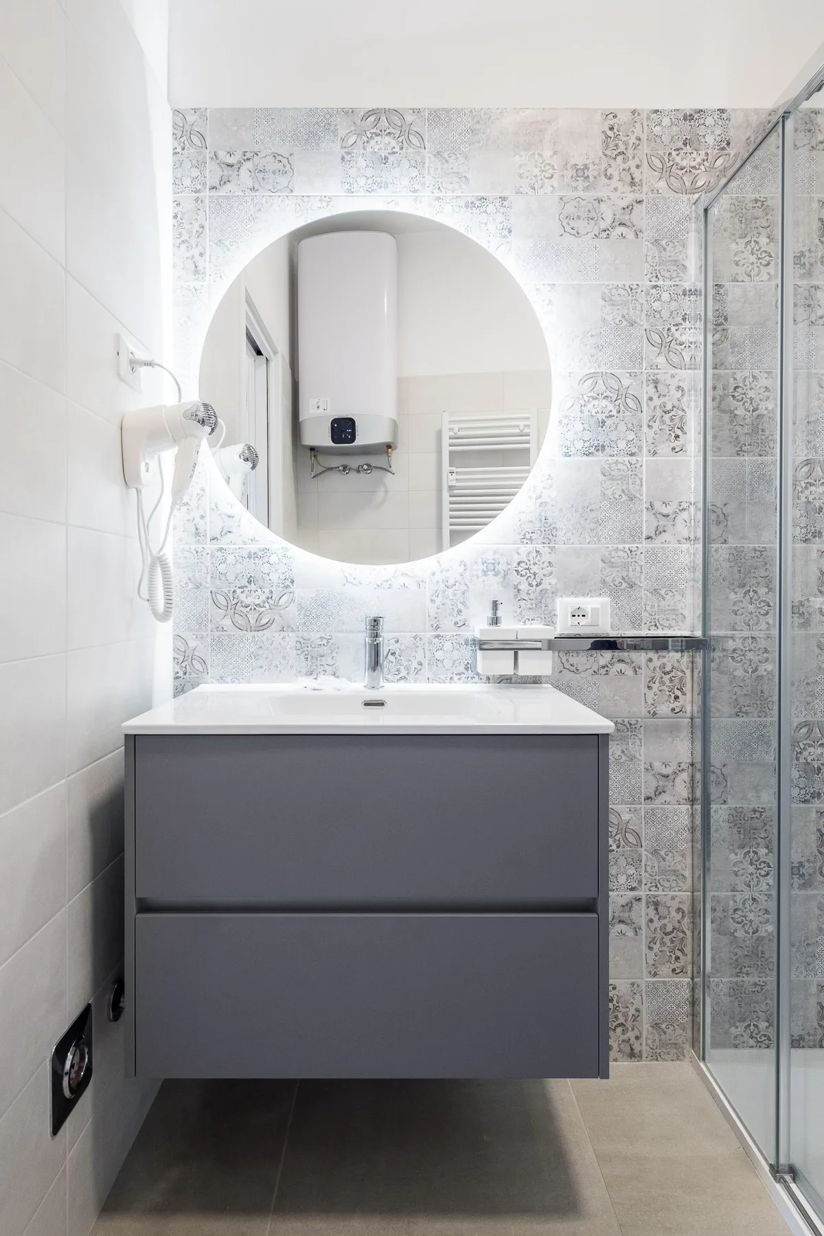 A modern bathroom features a gray vanity beneath a round mirror.