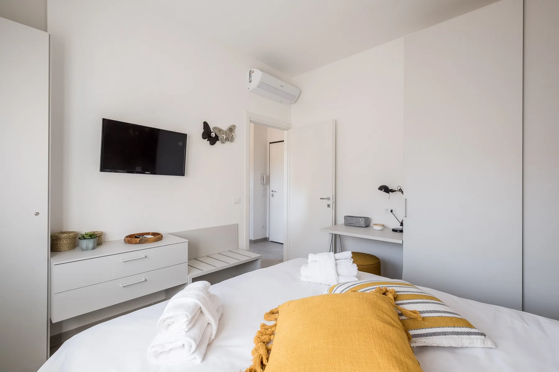 A bright bedroom with a bed, wall-mounted television, and desk.