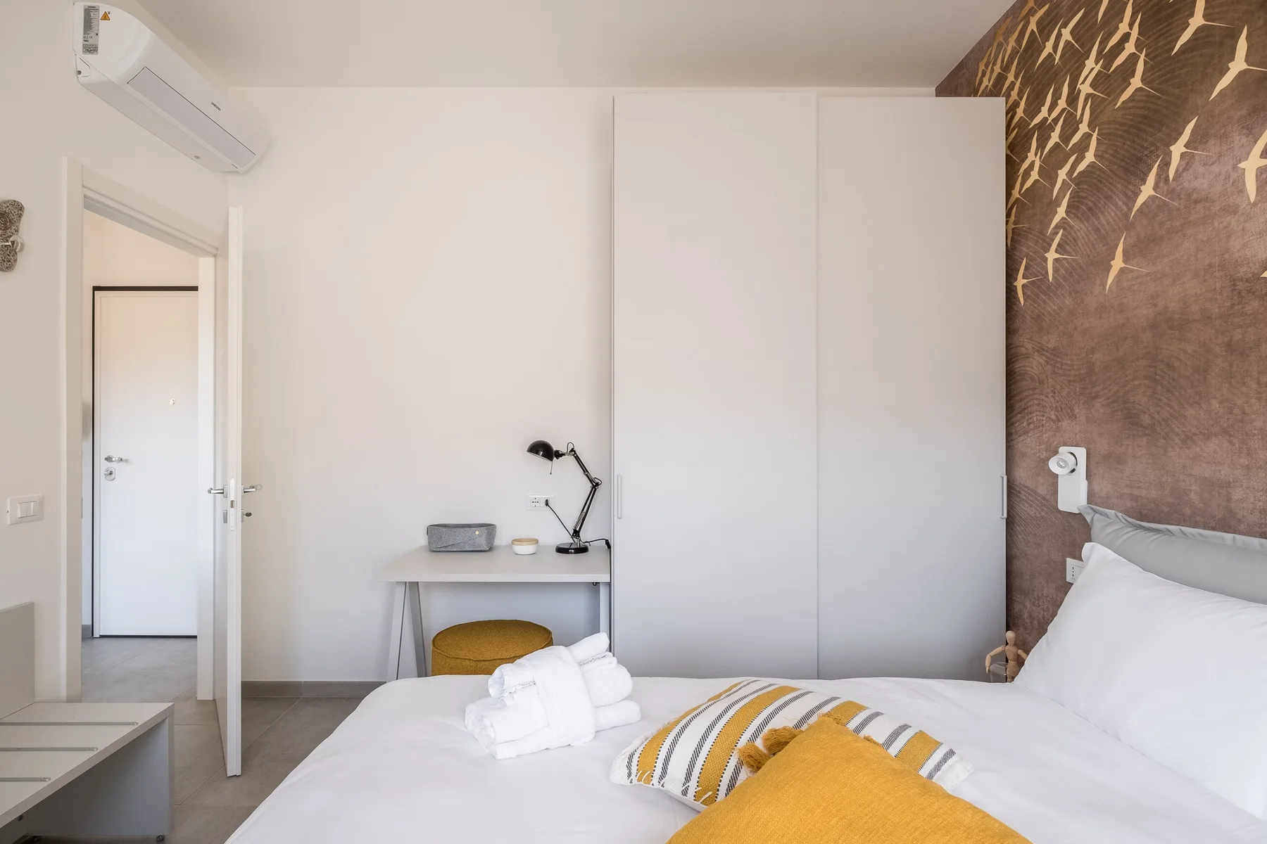 A bedroom with a bed, a small desk, and a patterned accent wall.