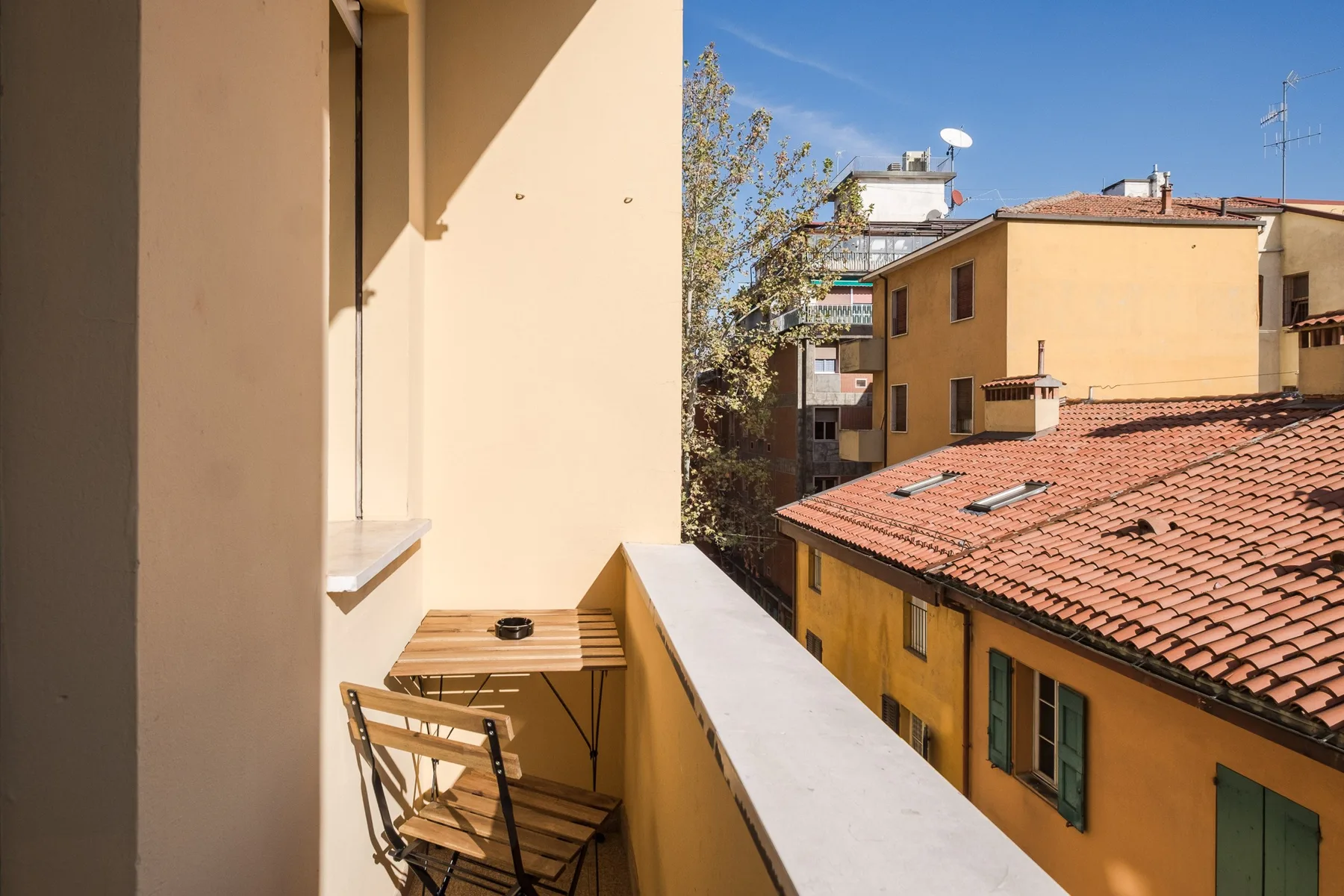A sunny balcony overlooks neighboring buildings and terracotta rooftops.