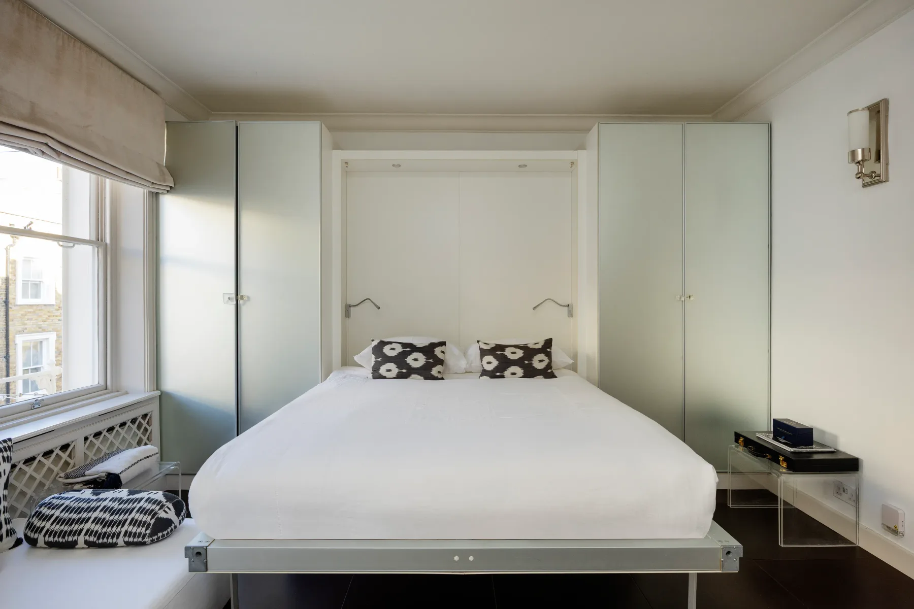 A bedroom with a neatly made bed between two tall wardrobes.