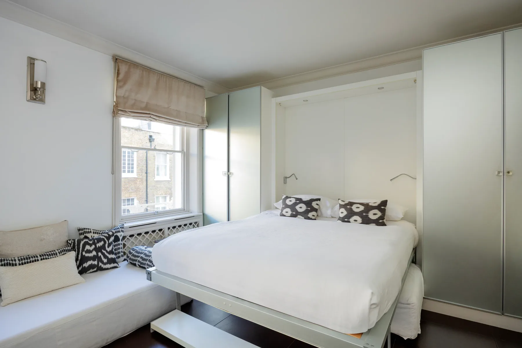 A bright bedroom with a white bed and a window with a shade.