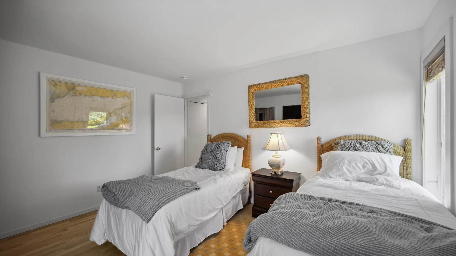 A bright bedroom with two beds, gray bedding, and a bedside table.