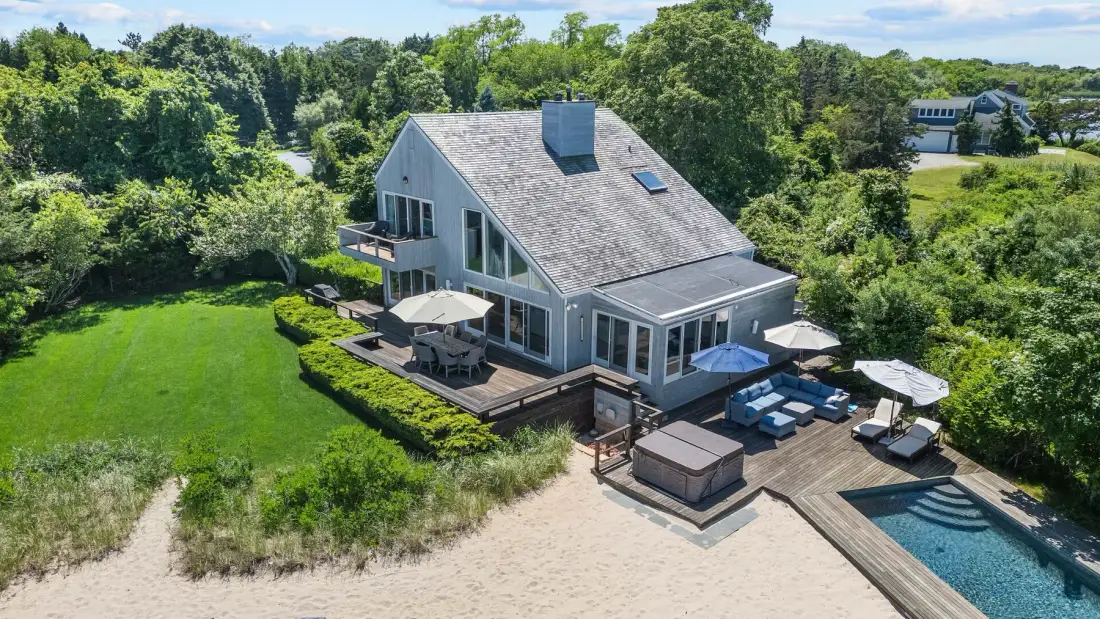 A house sits beside a sandy beach, with a deck and swimming pool.
