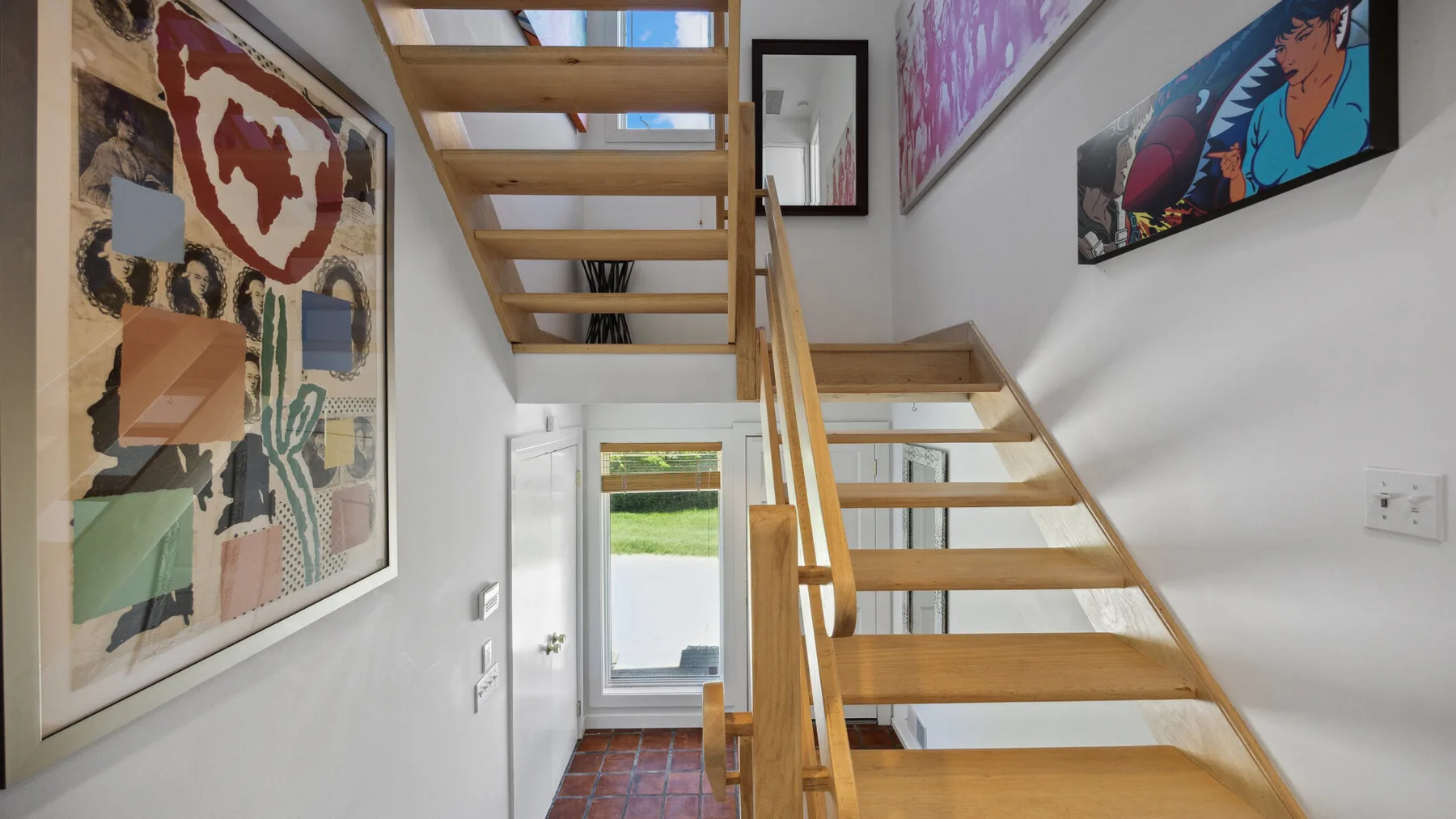 A bright interior hallway with a wooden staircase and framed artwork.