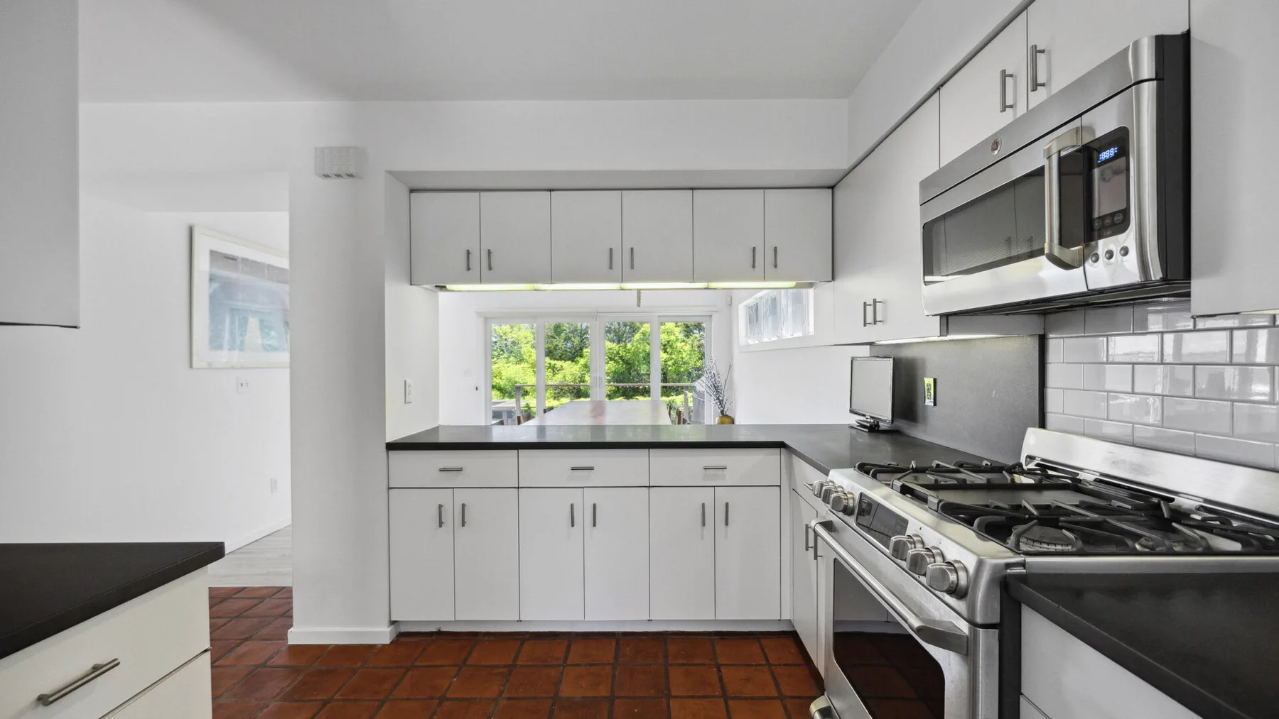 A bright kitchen with white cabinets, dark countertops, and stainless steel appliances.