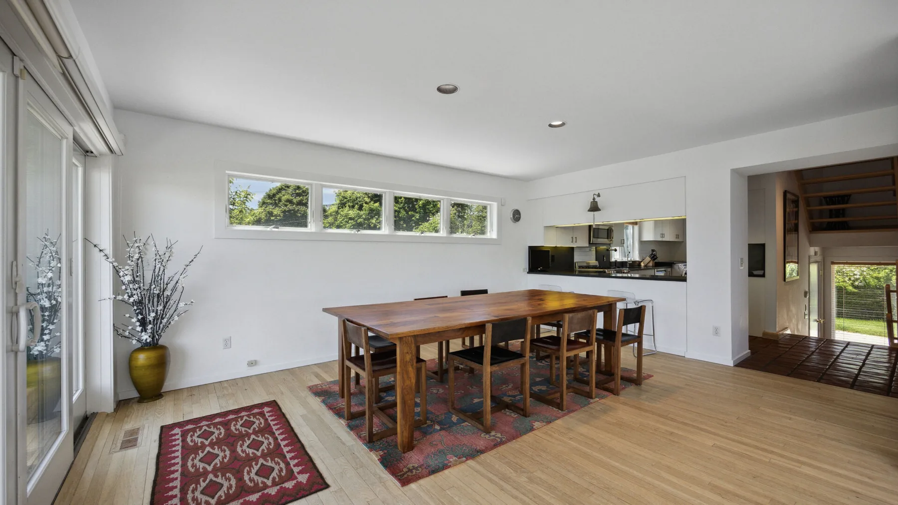 A bright dining area with a long wooden table and windows along one wall.