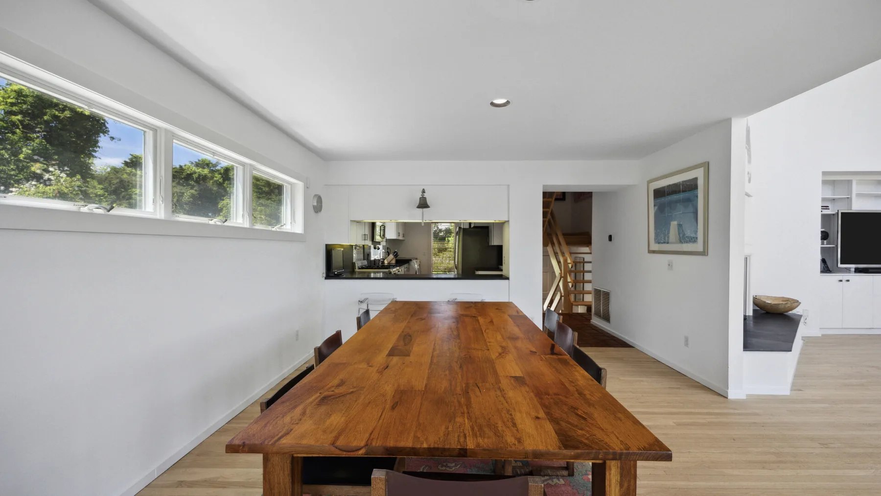 A dining area with a long wooden table and a kitchen visible beyond it.