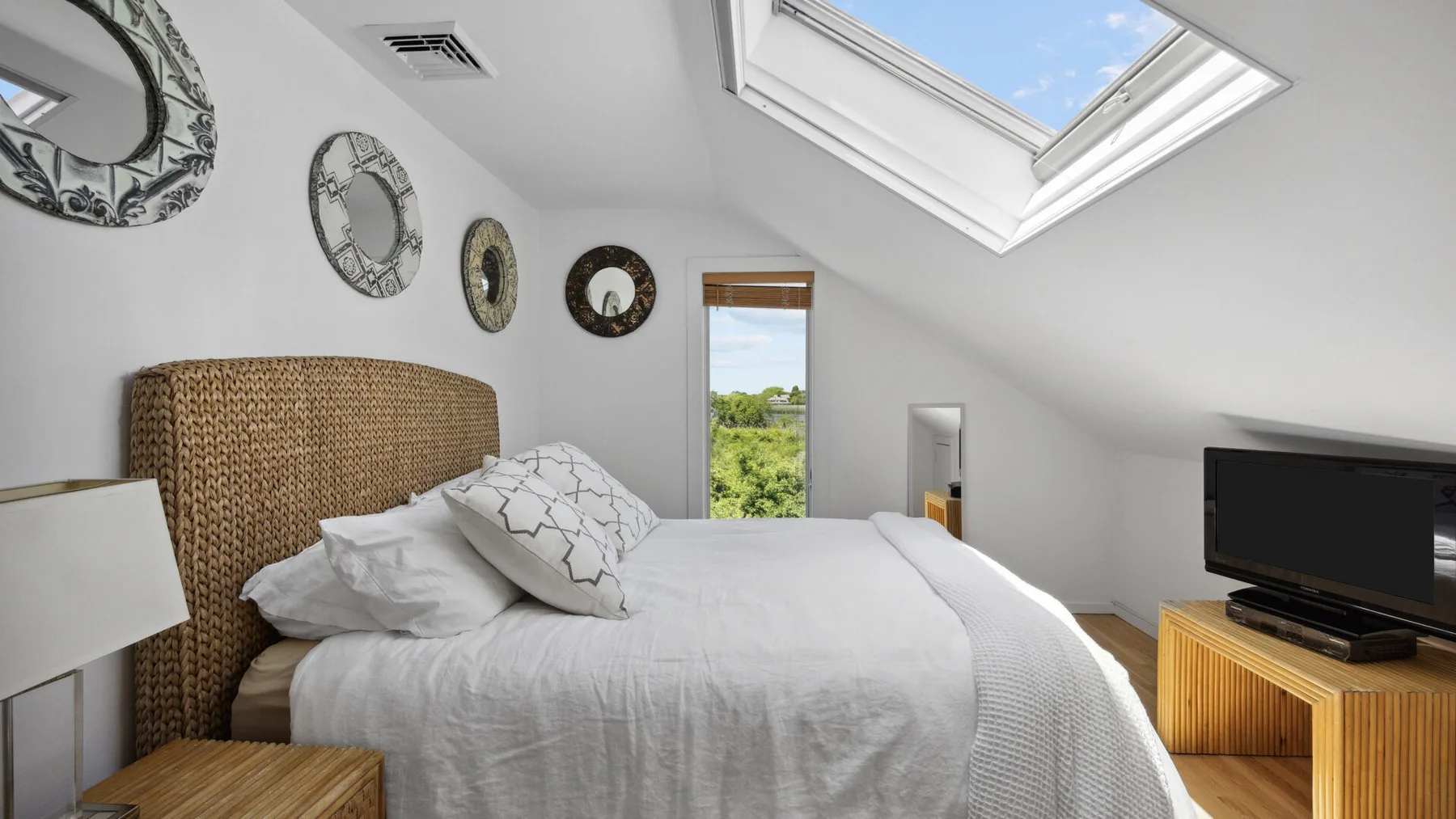 A bright attic bedroom with a bed beneath a large skylight.