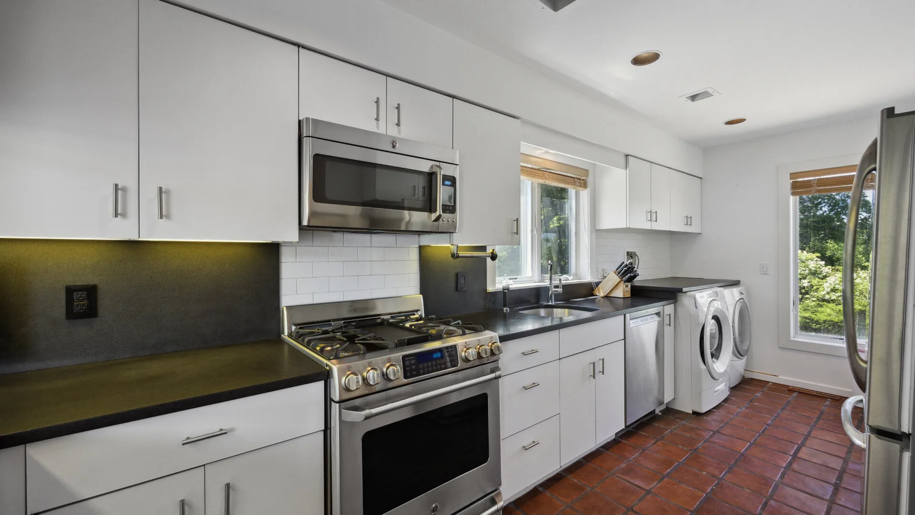 A bright kitchen with white cabinets, stainless steel appliances, and a tiled floor.