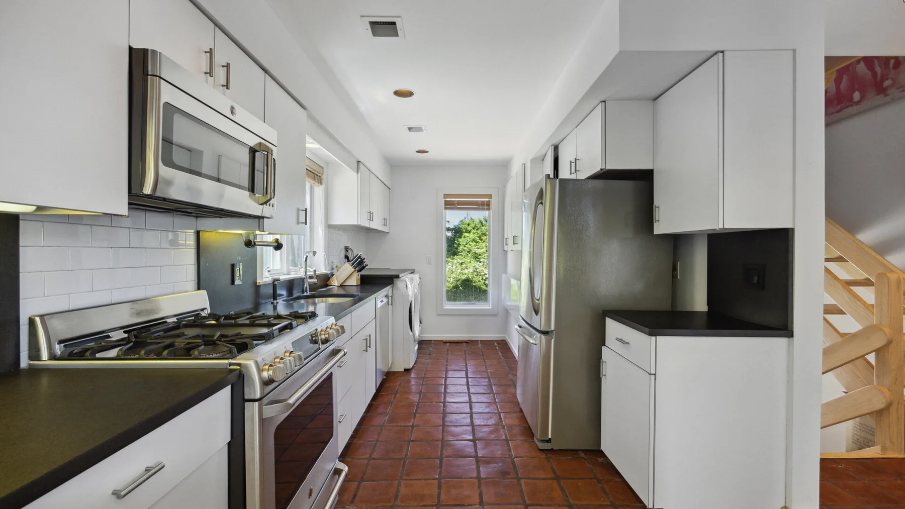A galley kitchen with white cabinetry, stainless steel appliances, and a tiled floor.