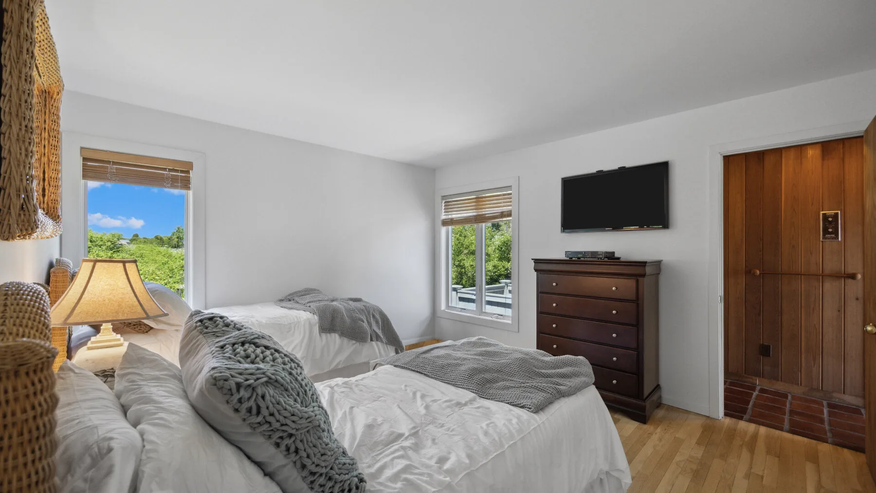 A bedroom with two beds, a dresser, and a television on the wall.
