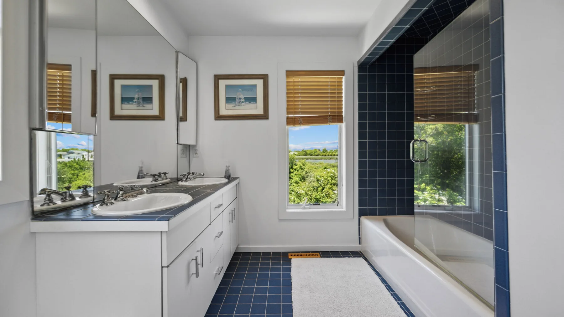 A bathroom with a long vanity and a tiled bathtub area beside a window.