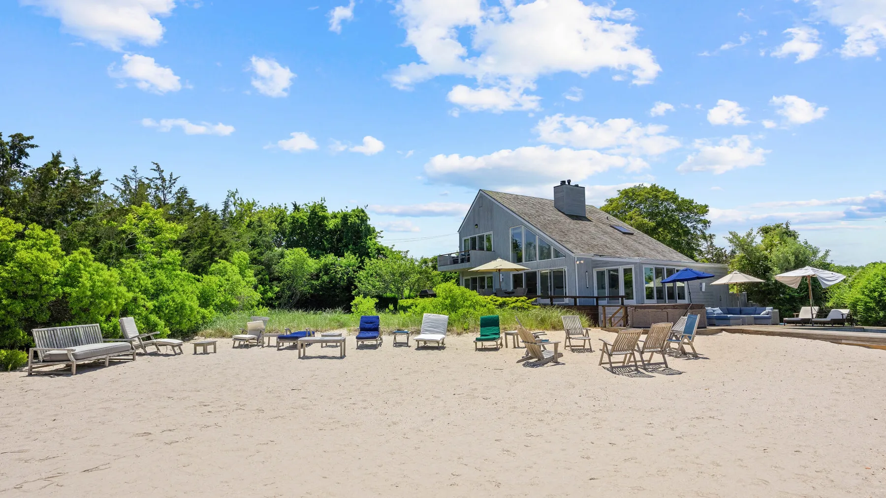A sandy outdoor seating area faces a large house beneath a bright blue sky.