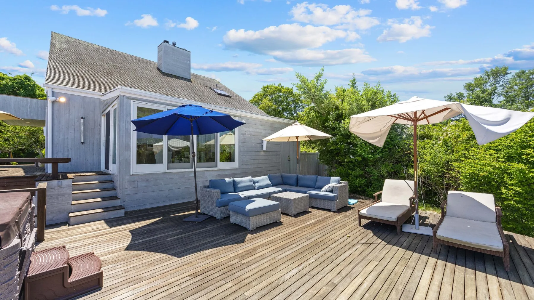 A wooden deck with outdoor seating, umbrellas, and a view of the house.