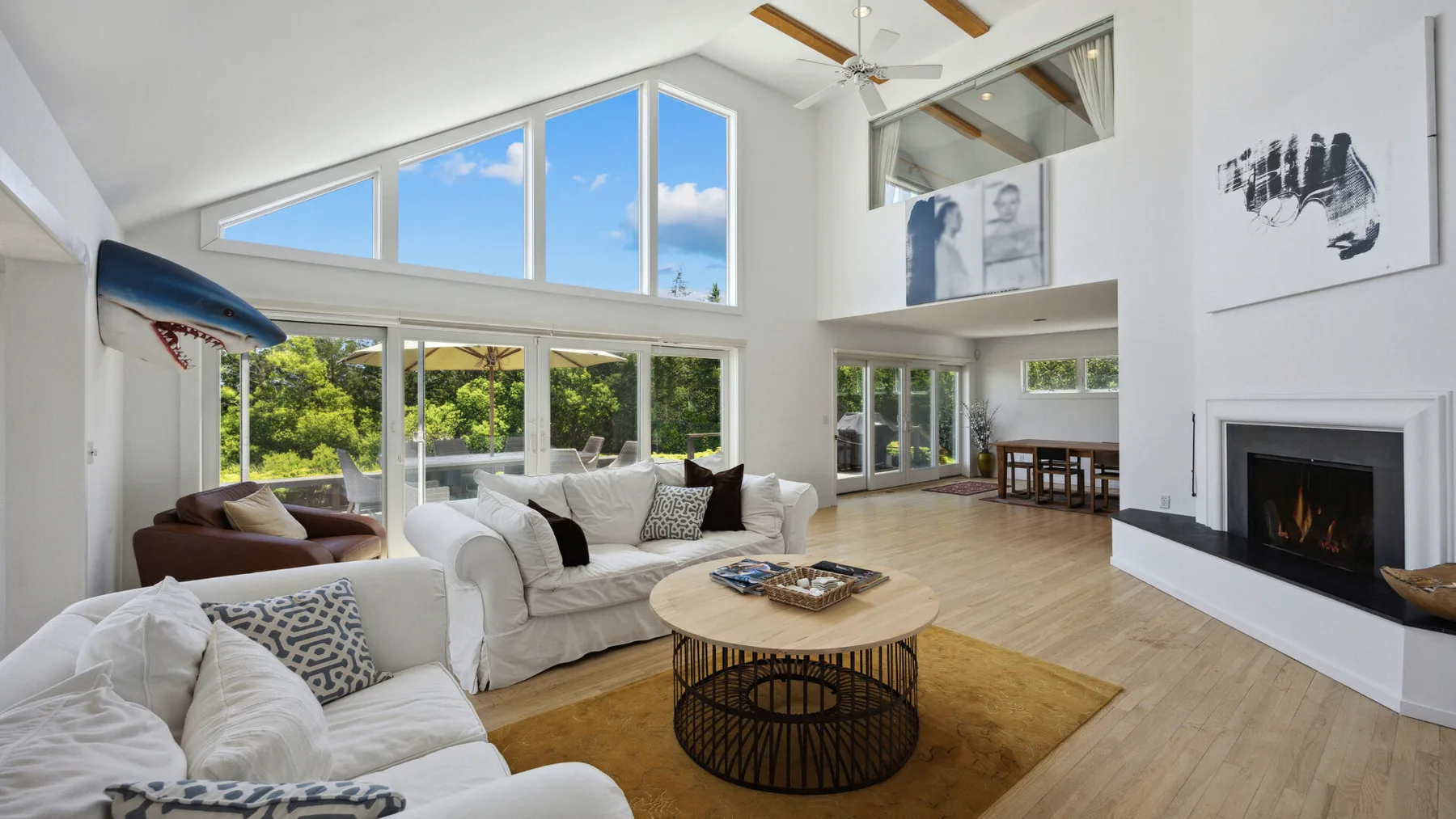 A bright living room with large windows, white seating, and a fireplace.