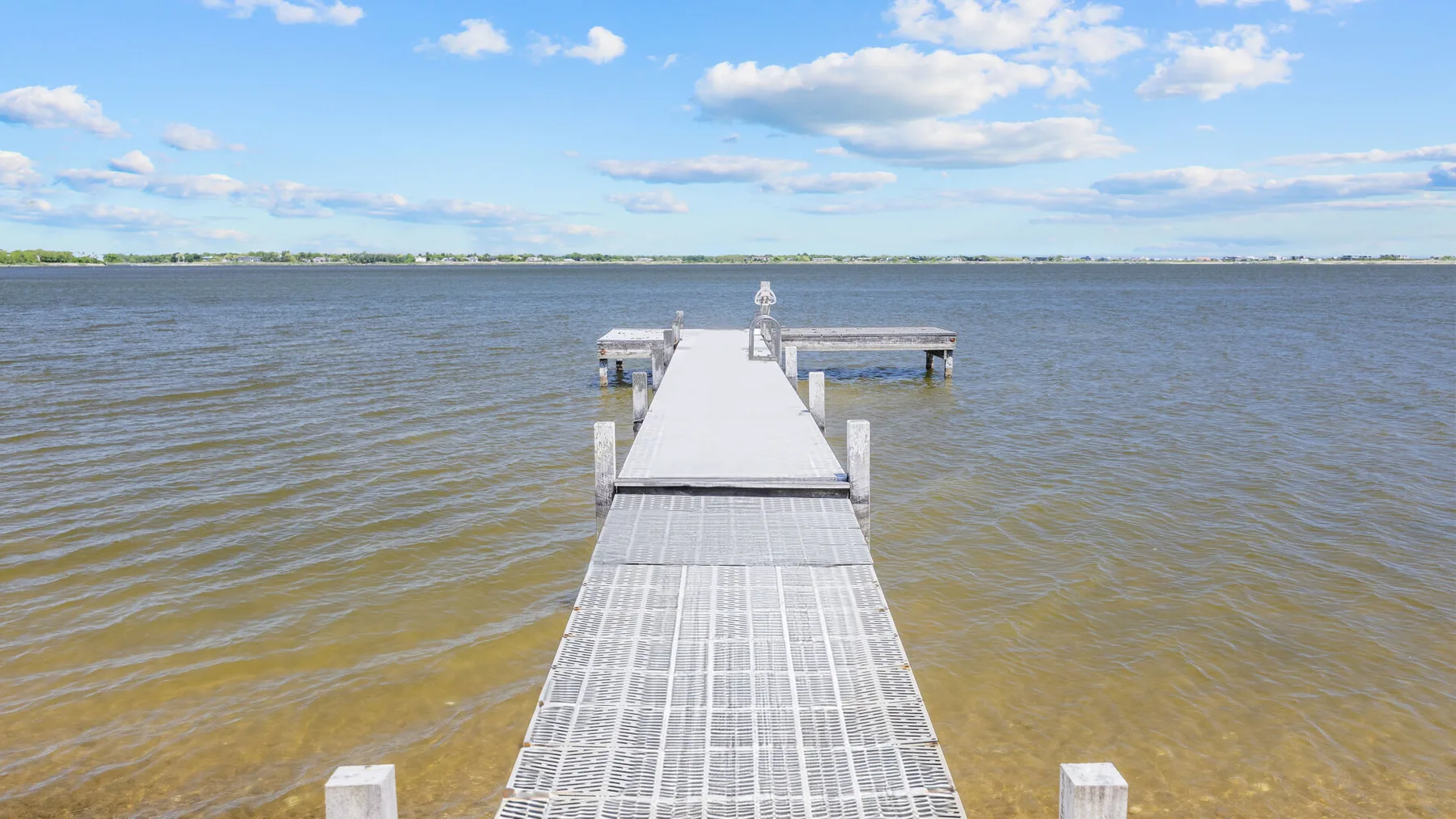 A long dock extends into a broad lake beneath a partly cloudy sky.