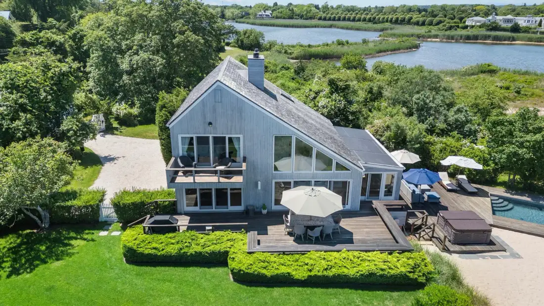 A lakeside house with a wooden deck and surrounding green lawn.