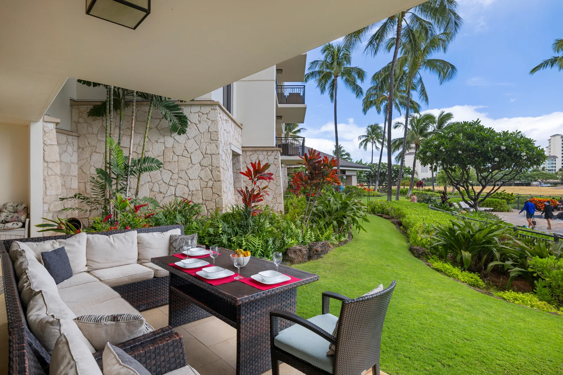 Un patio al aire libre con asientos acolchados y una mesa junto a un jardín cuidado.