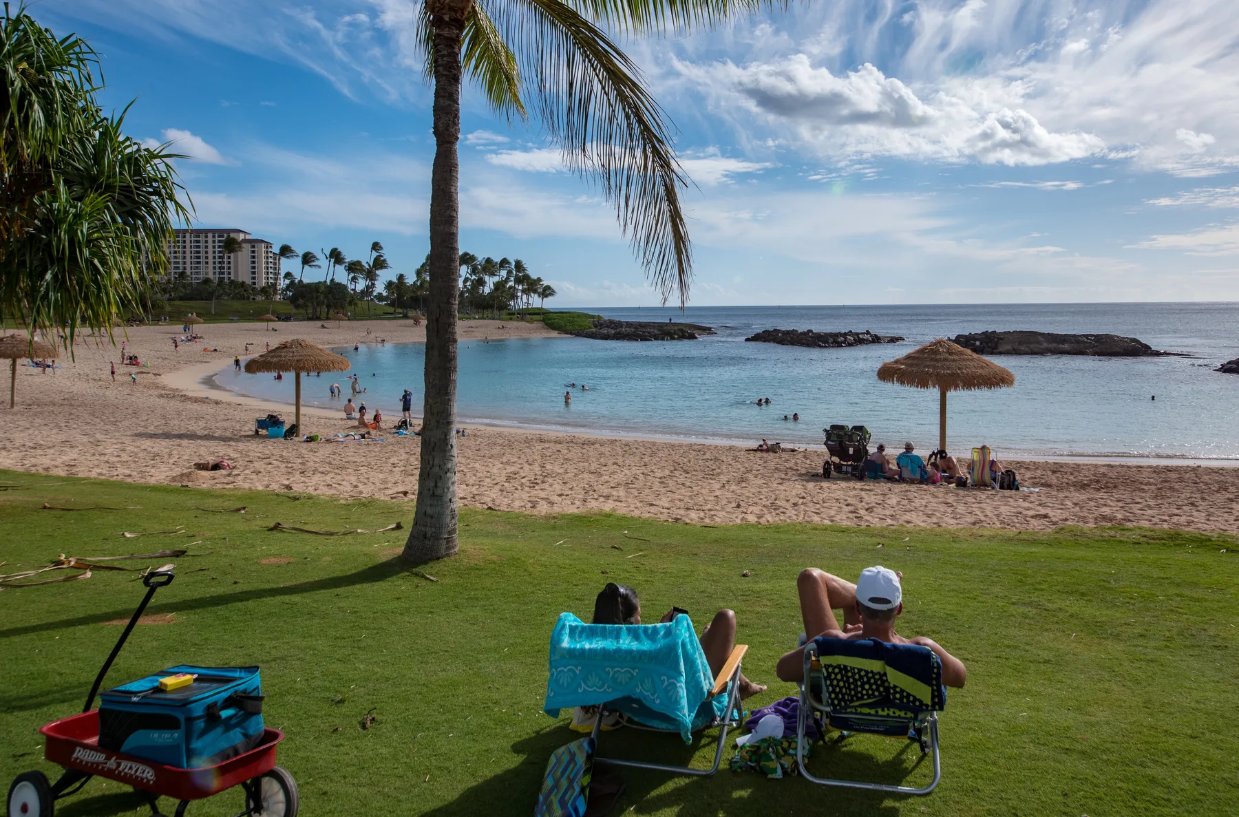 Una playa soleada con personas descansando en la arena y en sillas de playa.