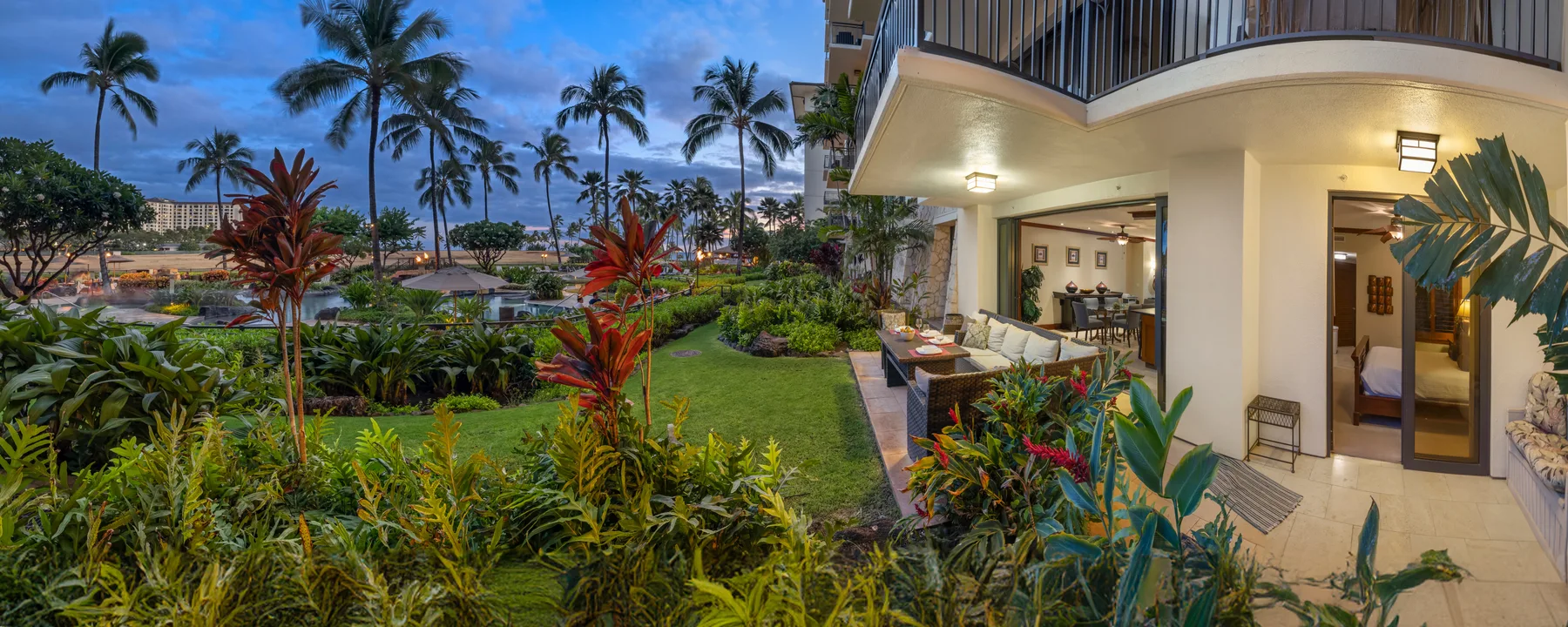 Un jardín tropical junto a un patio cubierto, con palmeras al fondo.