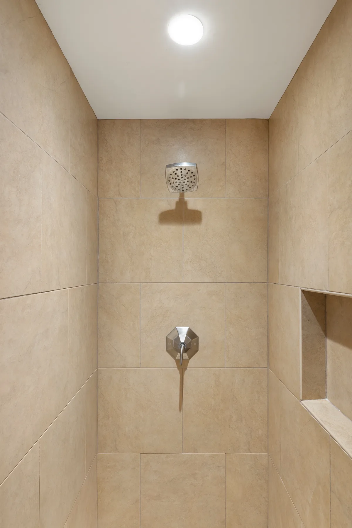 Una ducha con azulejos, rociador y control montados en la pared.
