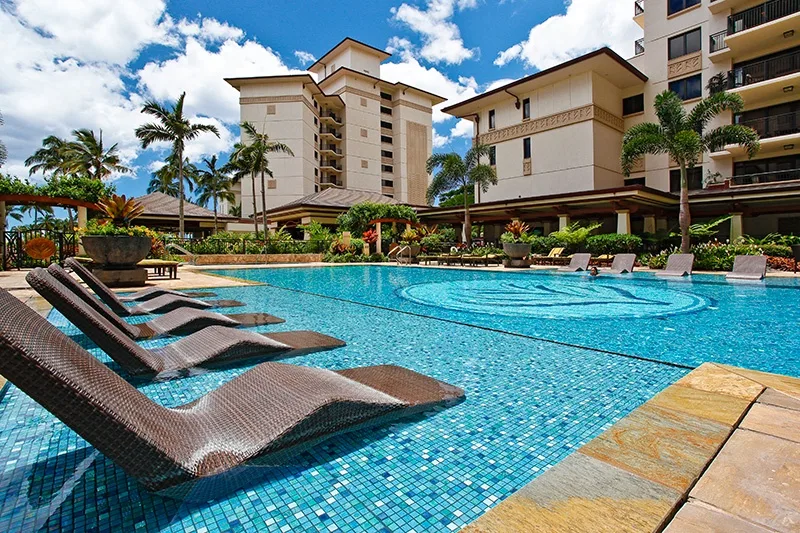 Una piscina está junto a edificios tipo resort, con tumbonas junto al agua.
