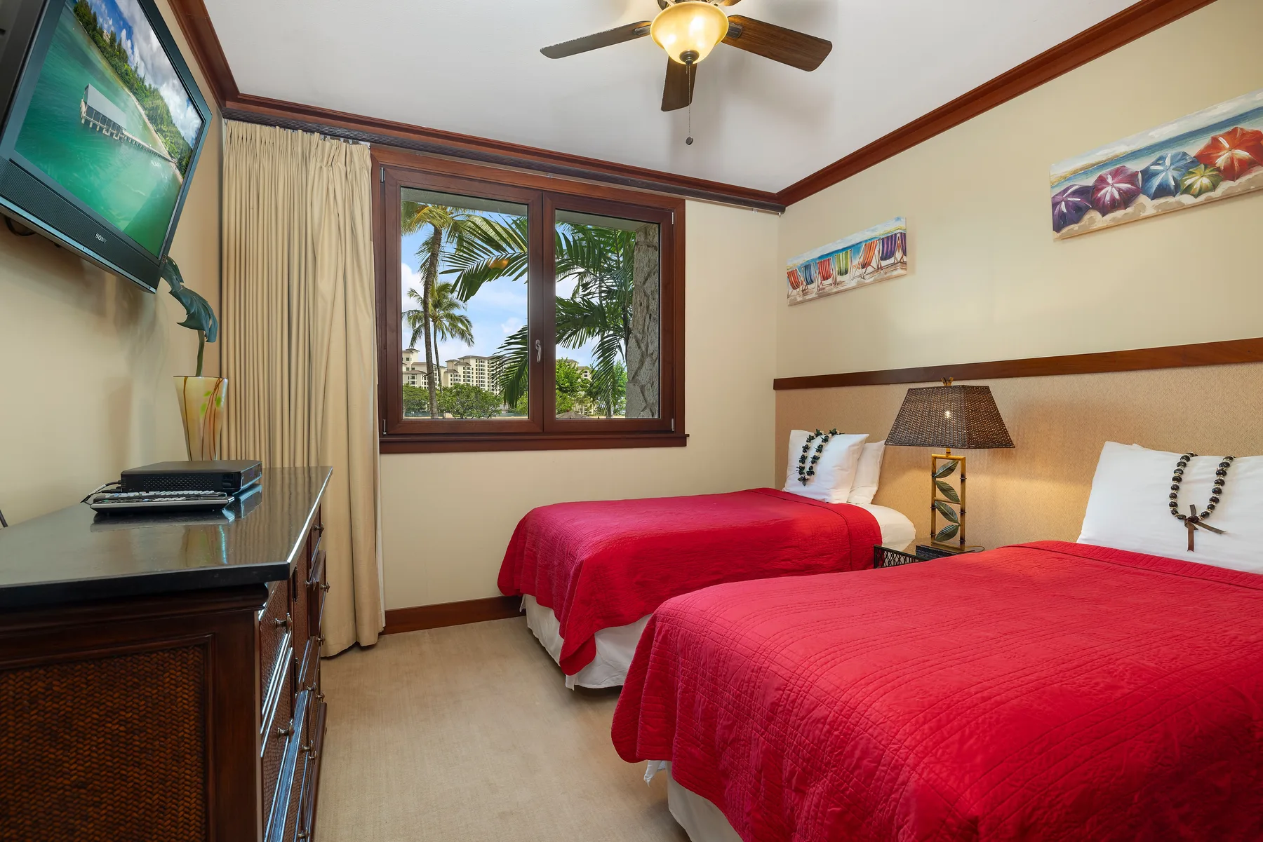 Un dormitorio con dos camas cubiertas con colchas rojas y una ventana con palmeras a la vista.