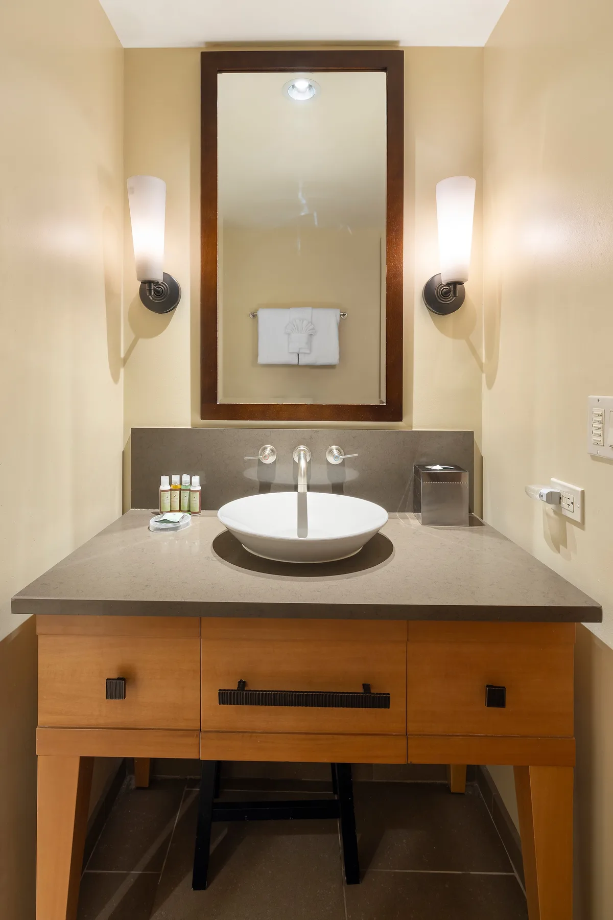 Un tocador de baño con lavabo sobre encimera está bajo un gran espejo enmarcado.