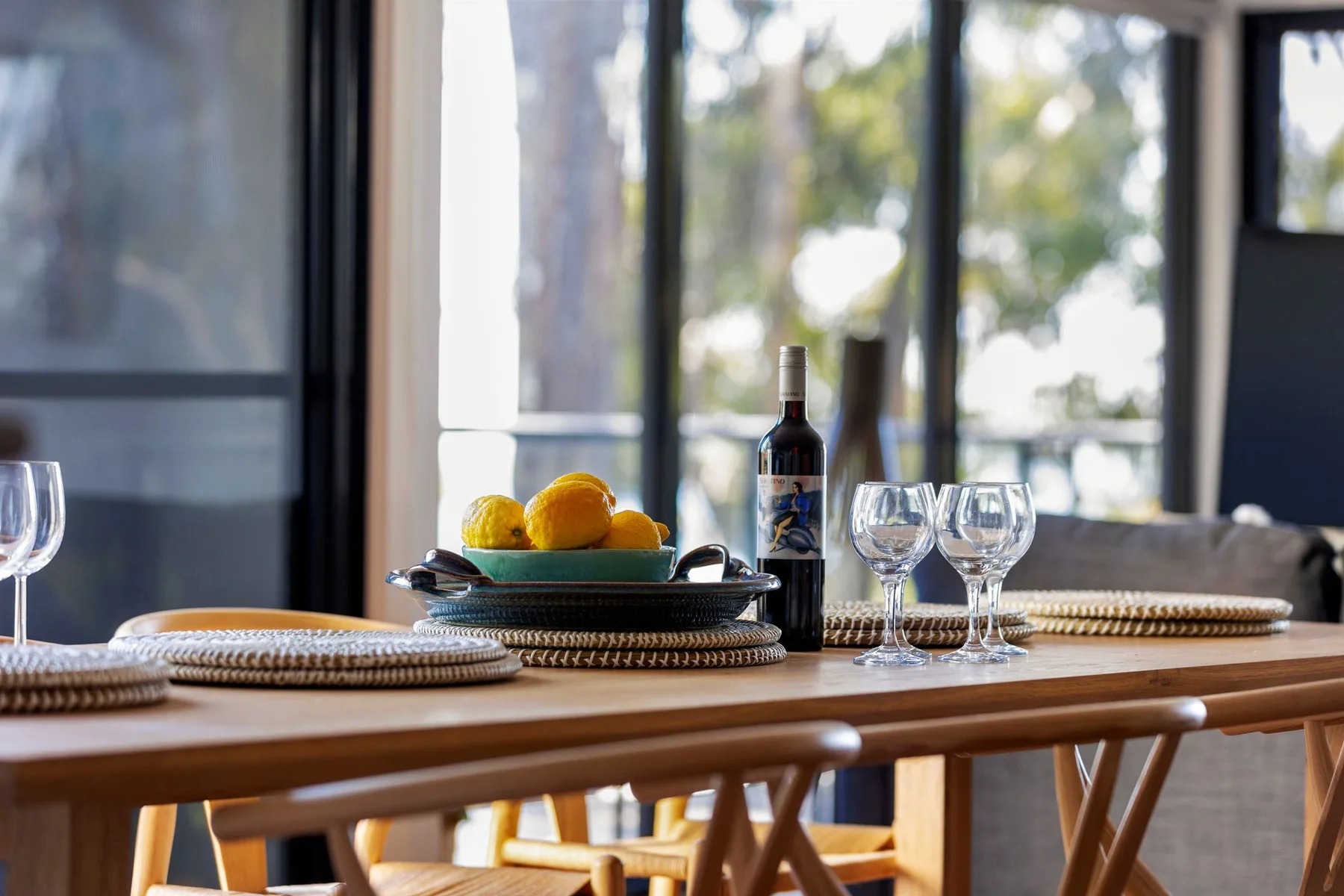 Una mesa de comedor está puesta con platos, copas y un cuenco de fruta.