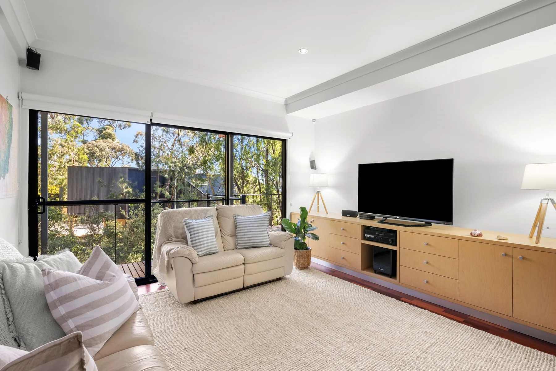 Una sala de estar luminosa con asientos, un televisor y ventanas grandes.