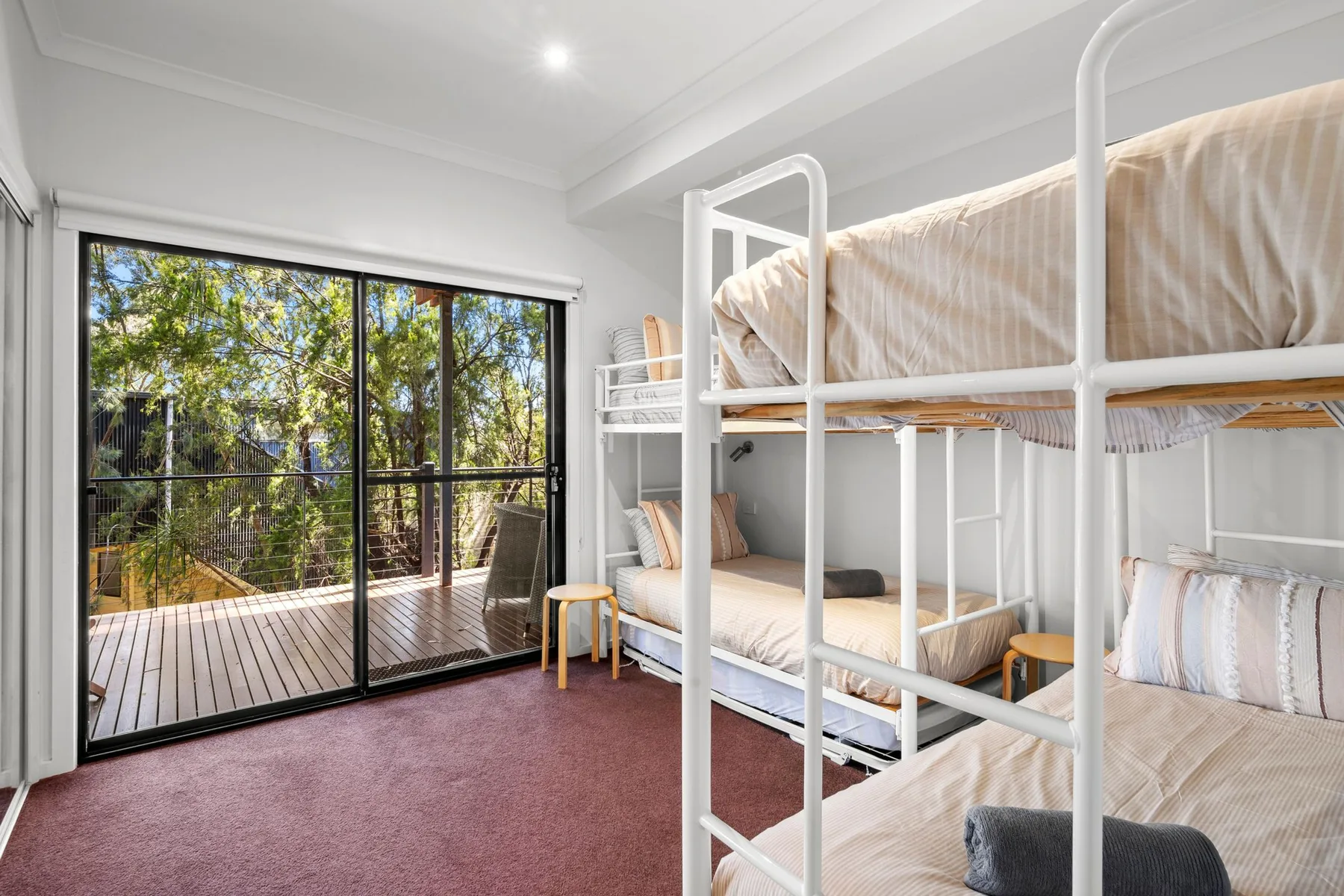 Un dormitorio luminoso con literas blancas y puertas corredizas de vidrio que dan a una terraza.