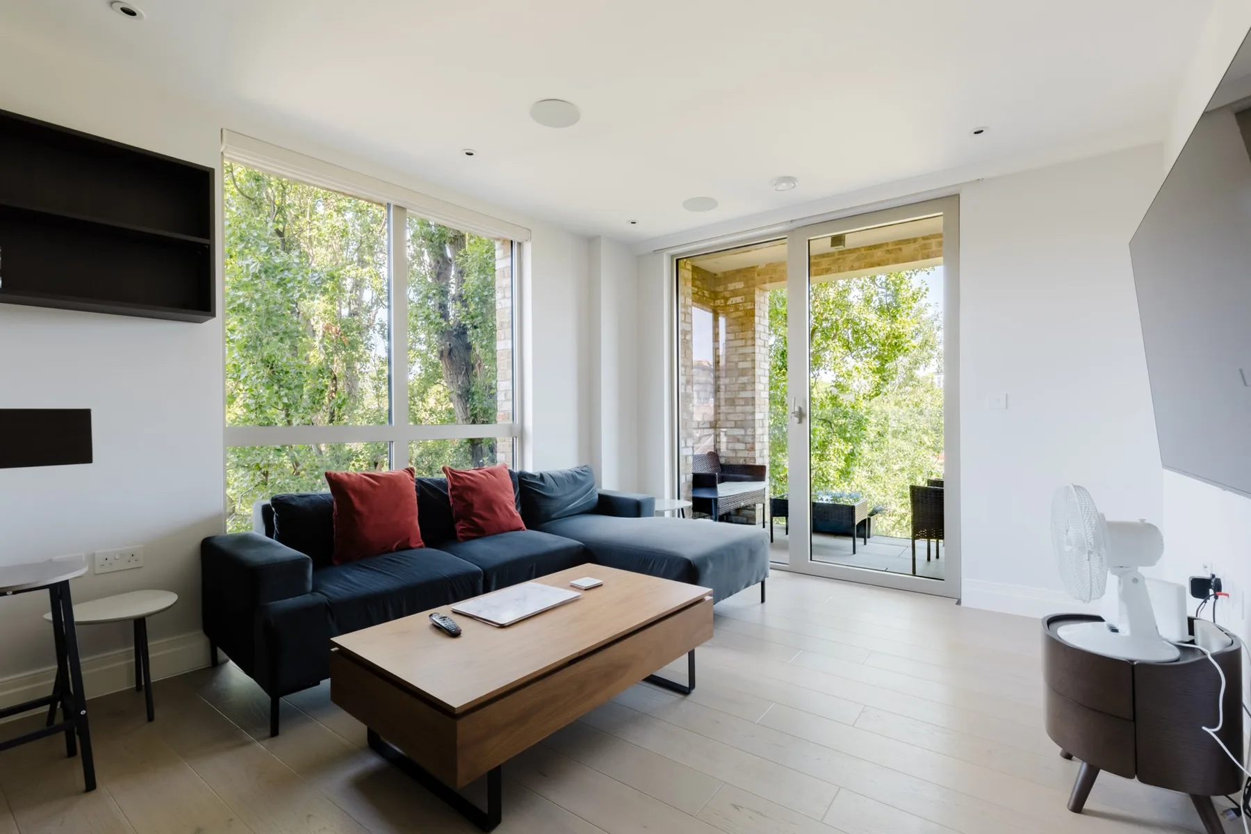 A bright living room has a dark sectional seating area beside large windows.