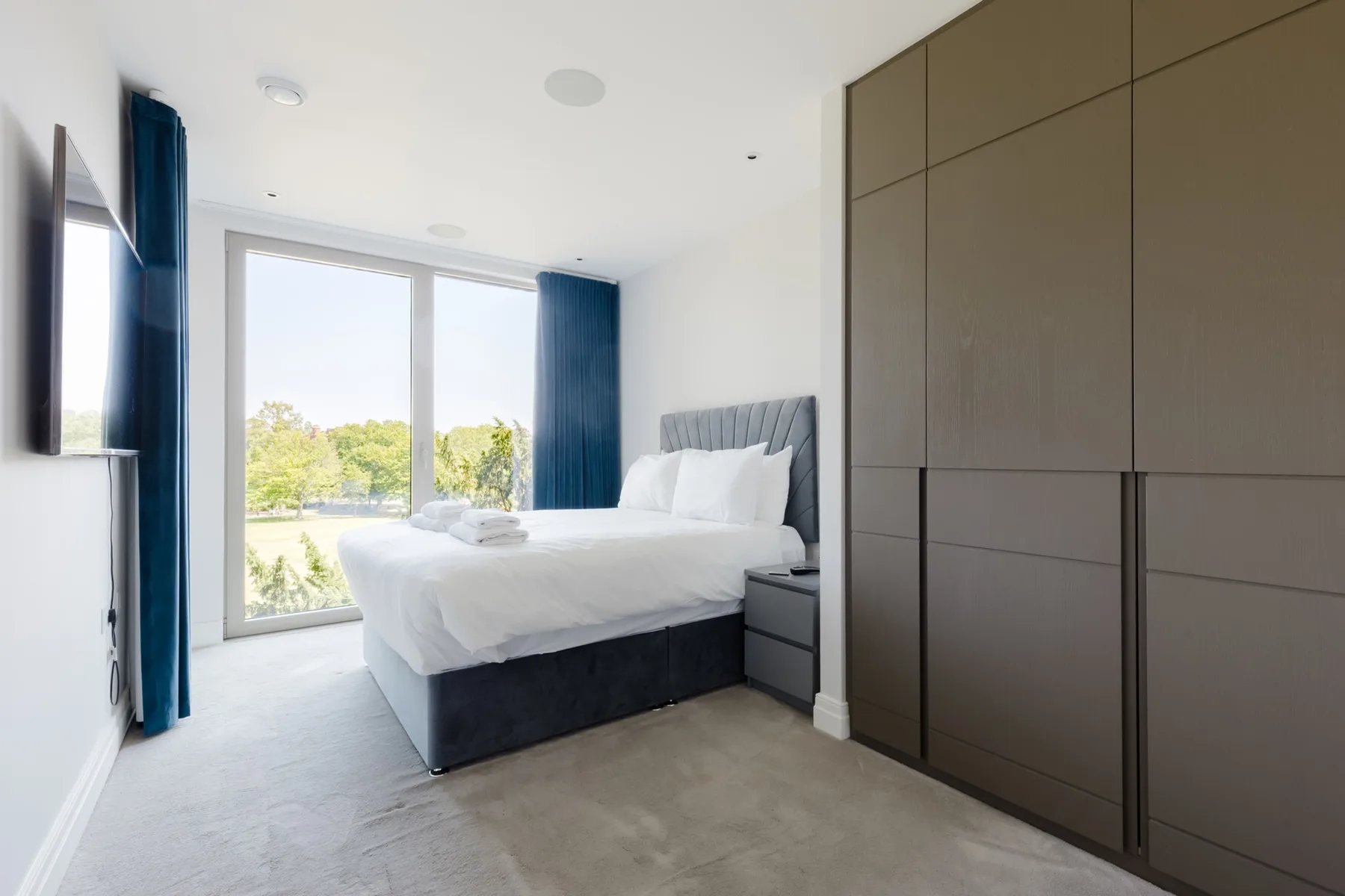 A bright bedroom with a neatly made bed beside large windows.