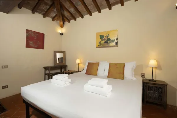 A bedroom with a large bed, folded towels, and bedside tables beneath exposed ceiling beams.