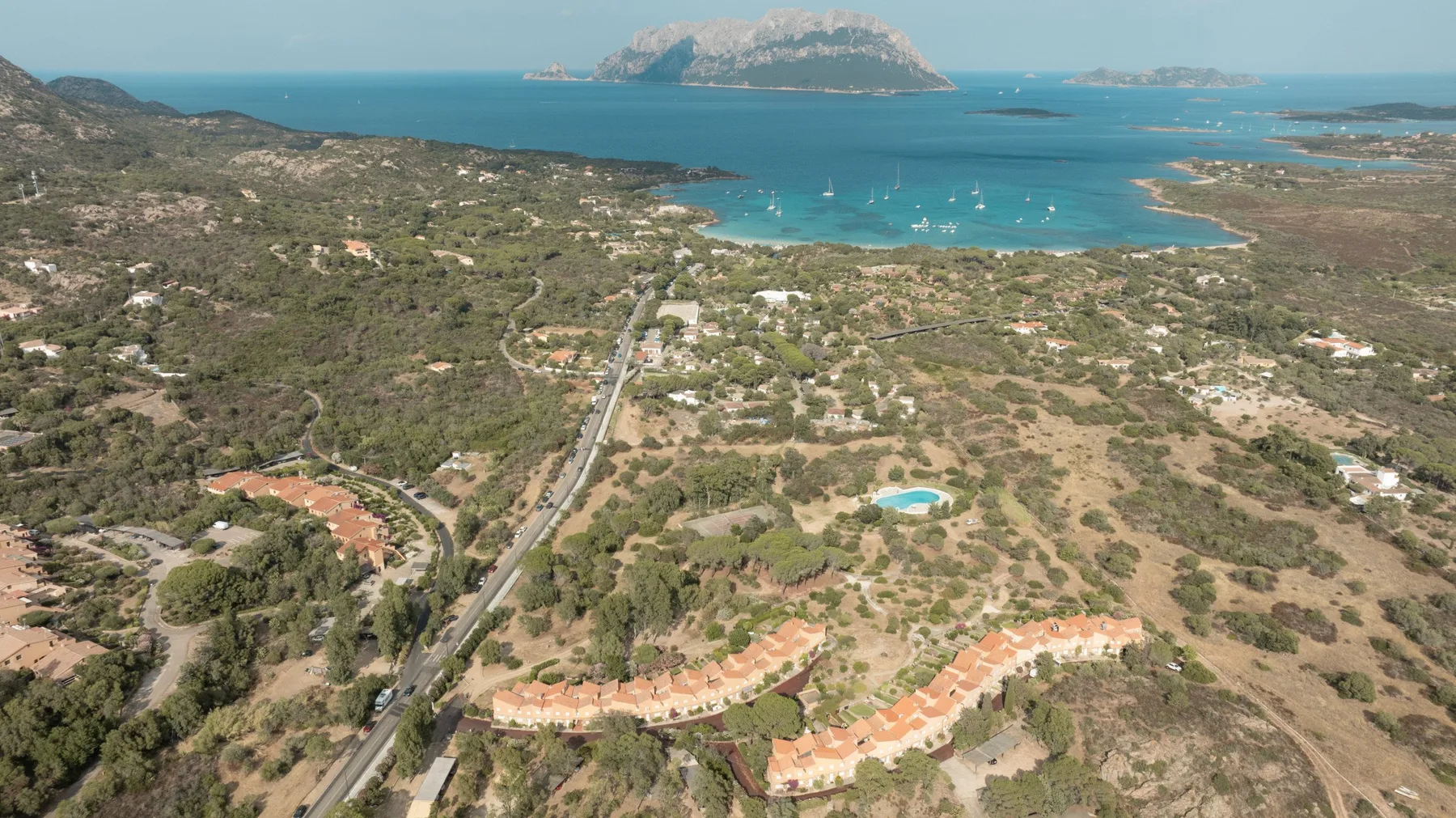 An aerial view of a coastal landscape with a winding road and turquoise bay.