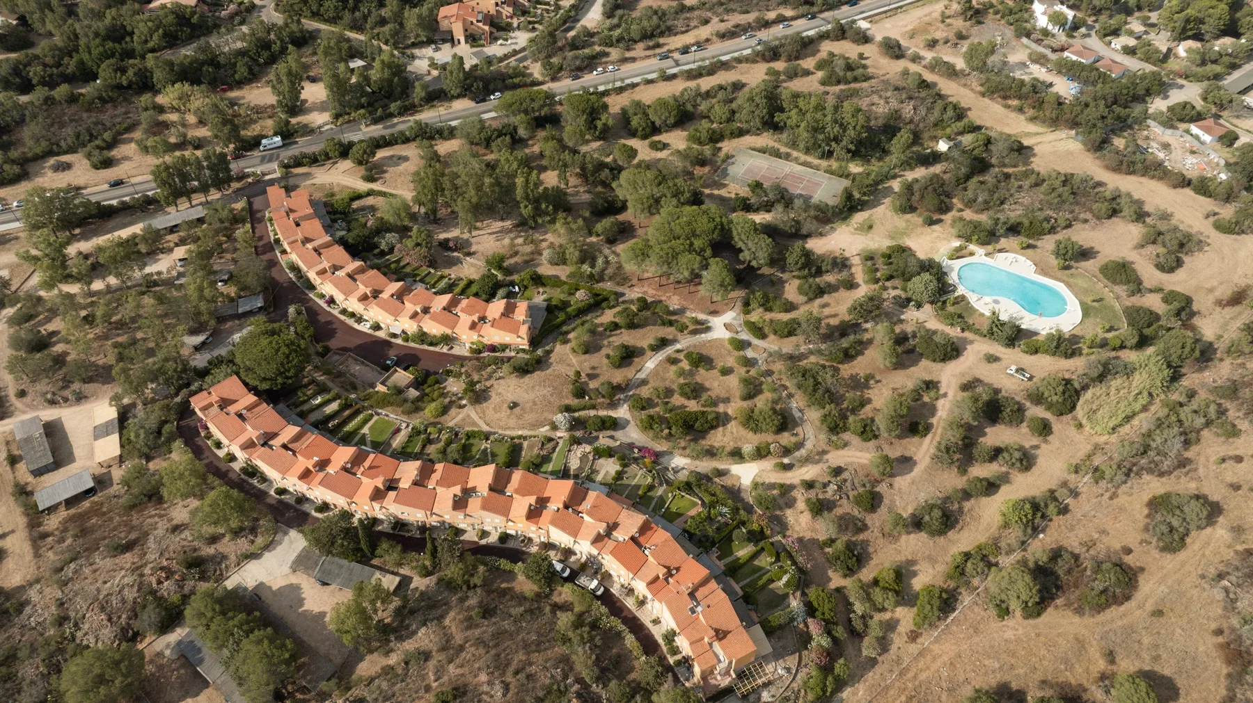 An aerial view of curved rows of buildings and a swimming pool among trees.