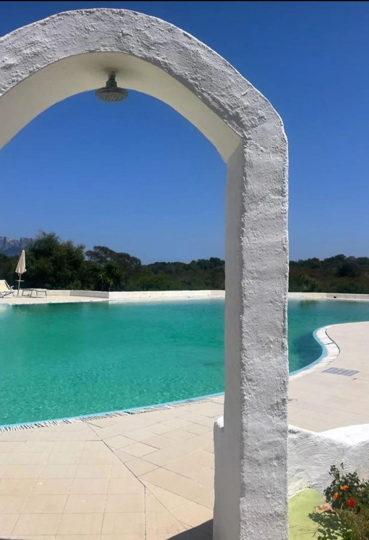 A turquoise swimming pool and tiled deck are framed by a white arch.